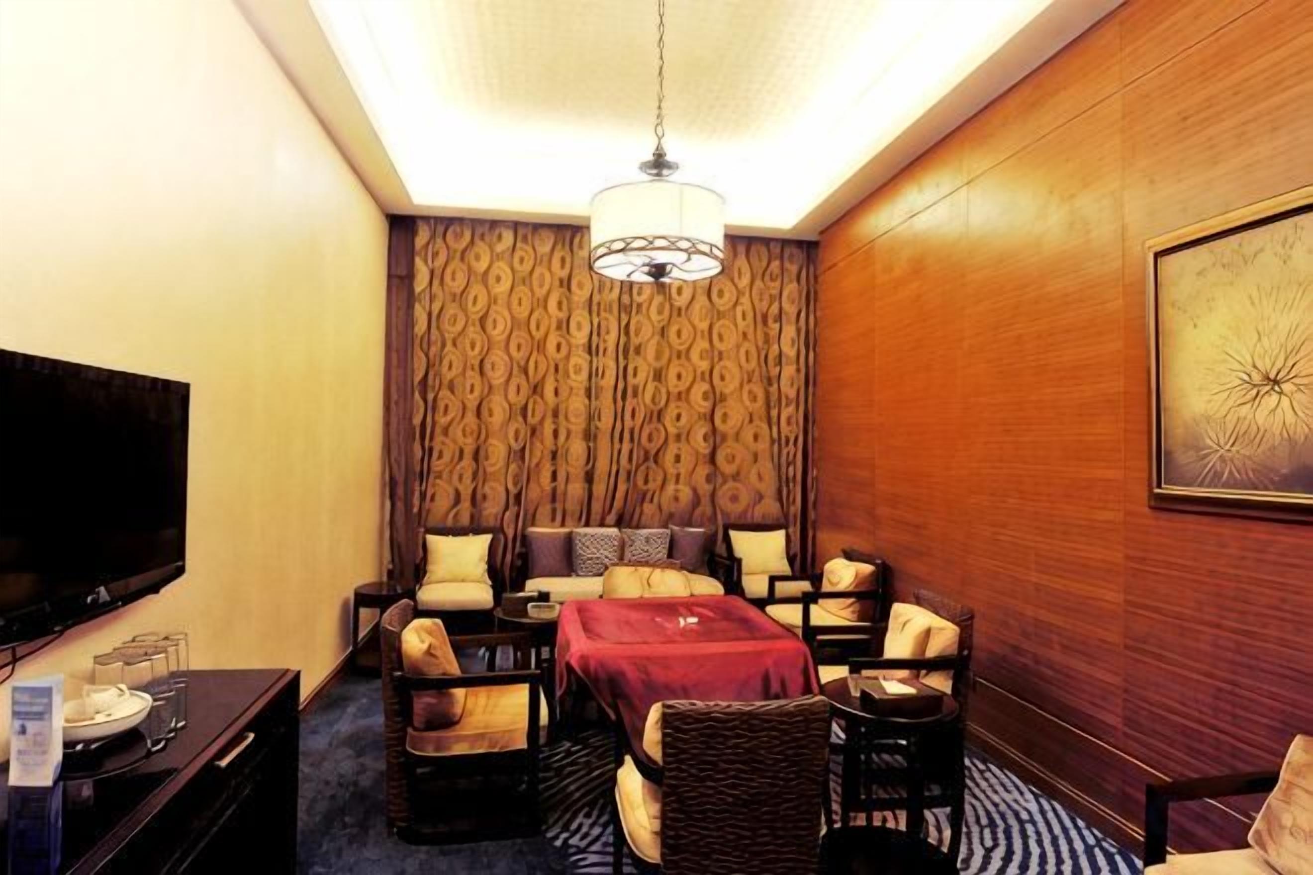 A hotel room with a flat-screen TV, a sofa set, a dining table, and a patterned wallpaper.