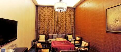 A hotel room with a flat-screen TV, a sofa set, a dining table, and a patterned wallpaper.