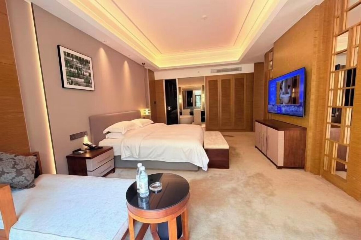 A hotel room with a bed, bedside table, and a TV on the wall.