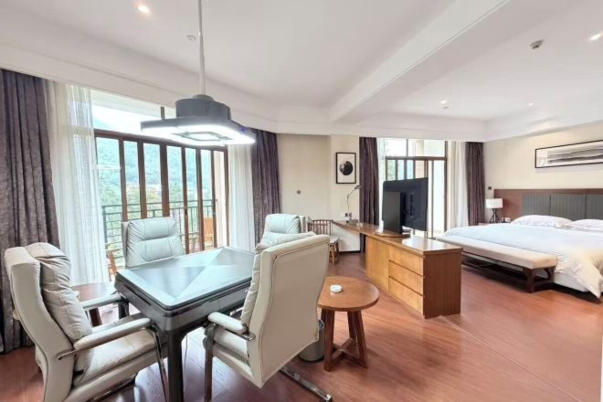 A hotel room with a dining table, two chairs, a bed, a TV, and a small side table.