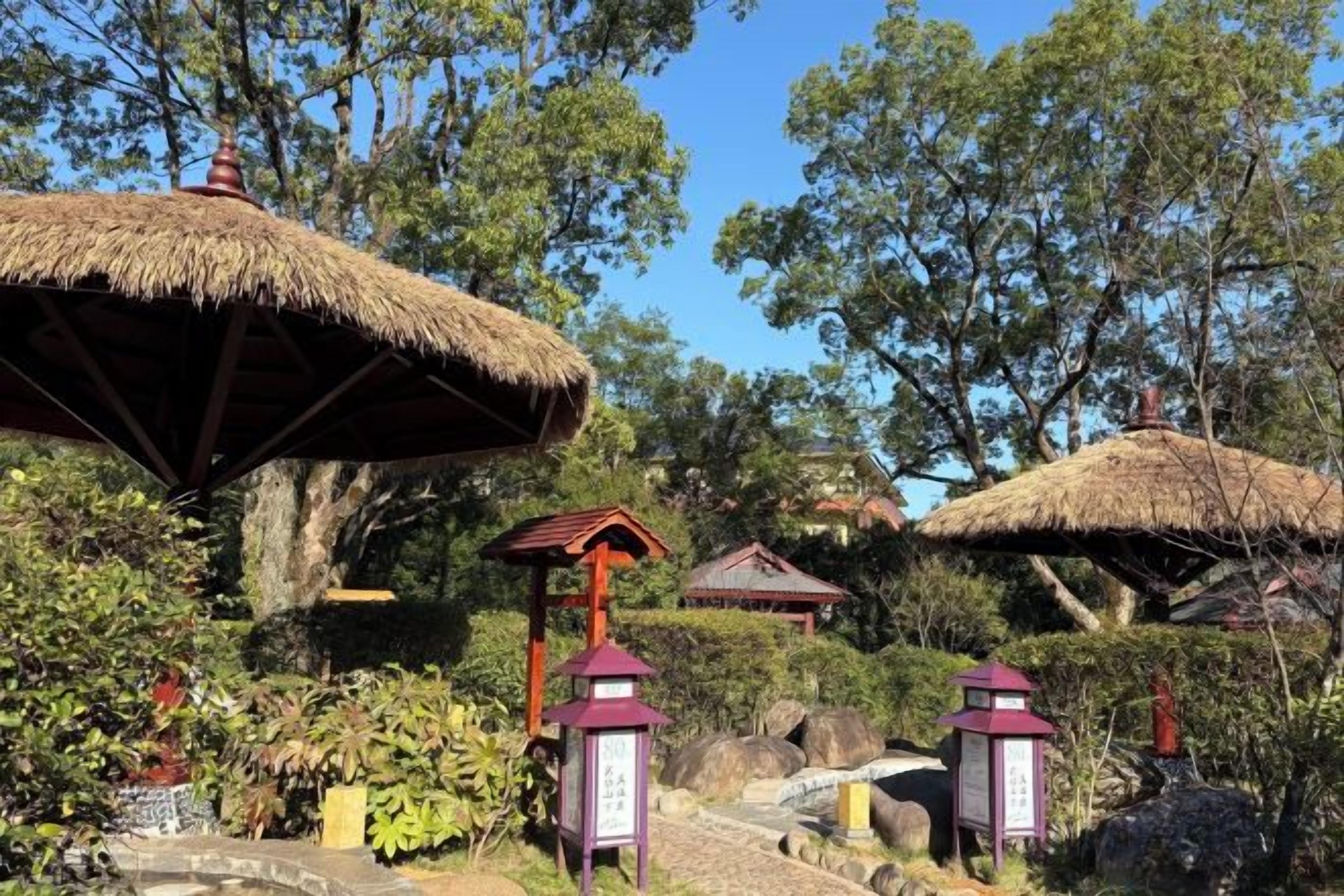 A garden with thatched-roof structures, stone lanterns, and lush greenery.
