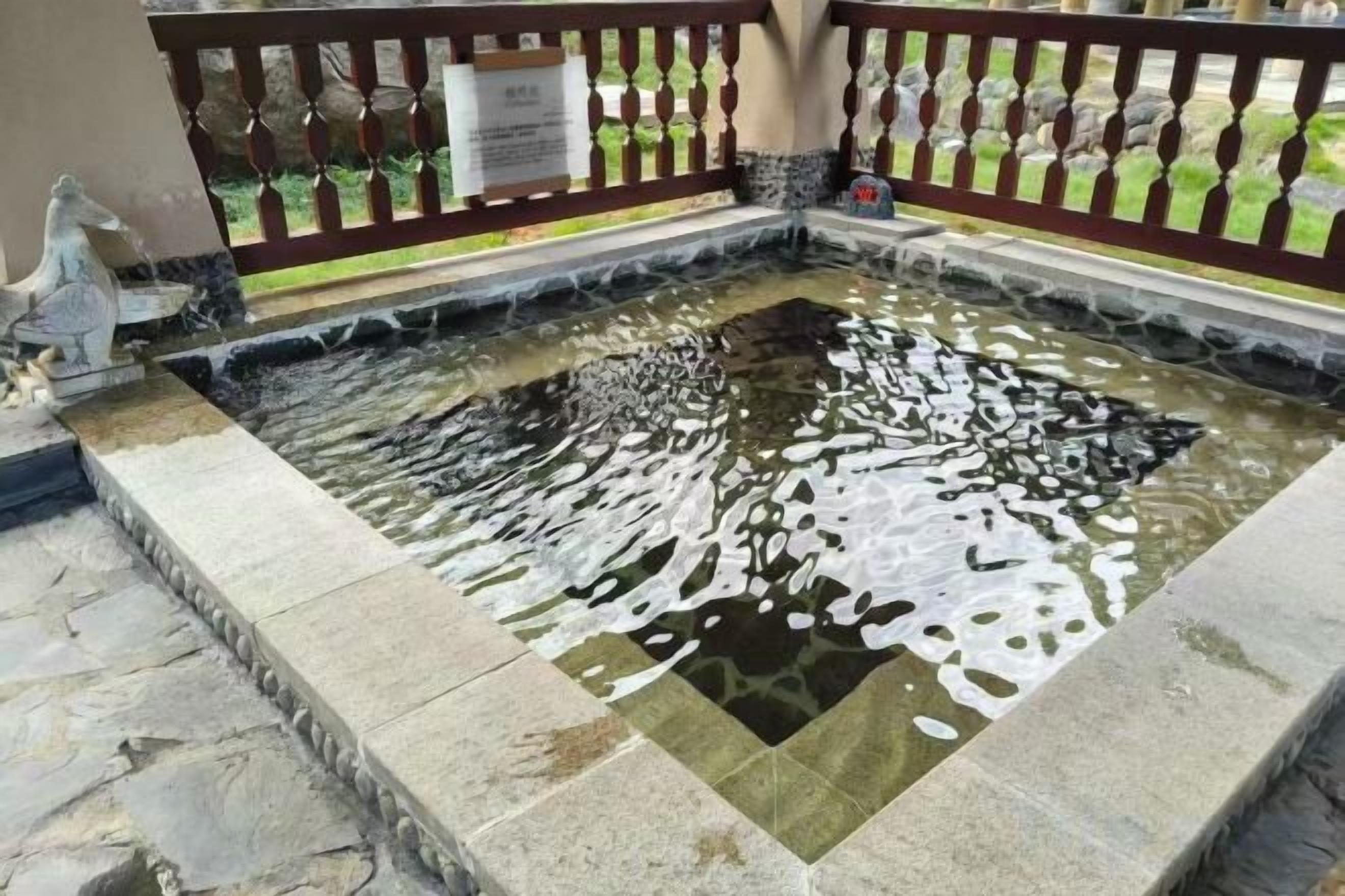 Un bassin d’eau de forme carrée, bordé de pierres et entouré d’une clôture en bois.