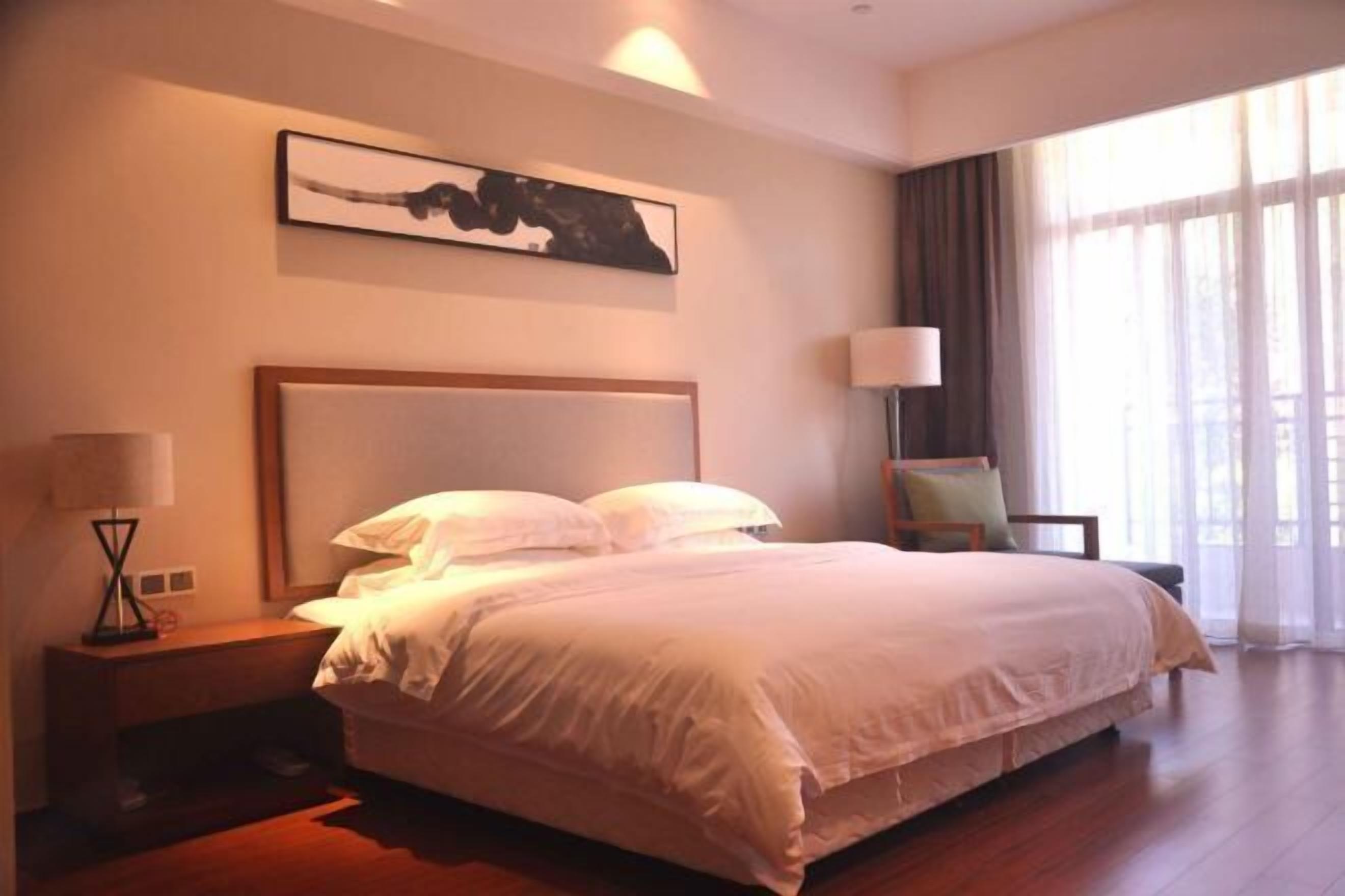 Una cama bien hecha en una habitación de hotel, con cabecera, lámpara de noche y una silla.