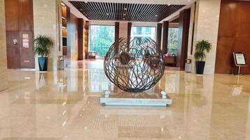A lobby with a central spherical sculpture, potted plants, and a polished floor.