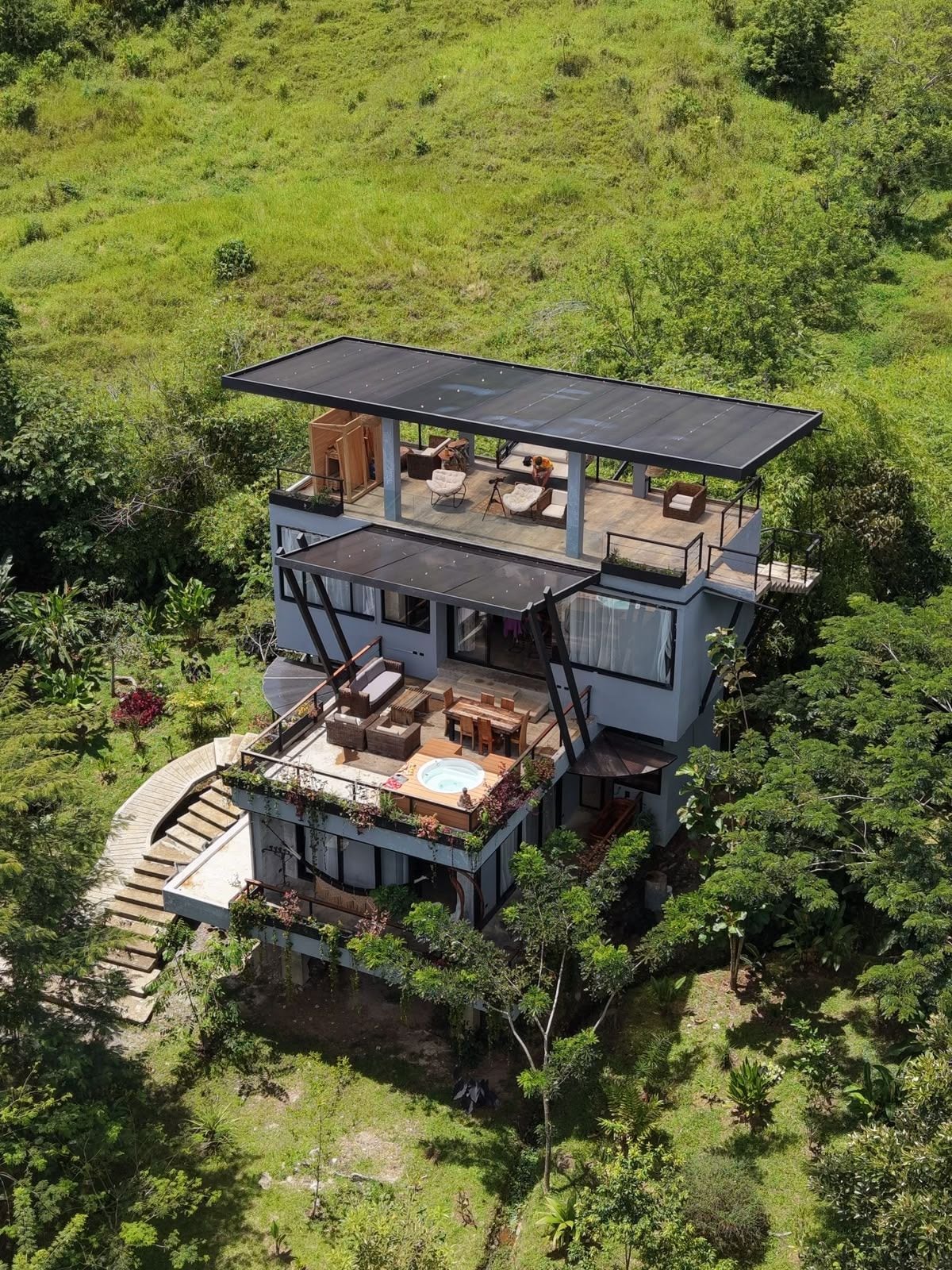 A modern two-story house with a flat roof, outdoor seating area, and a hot tub.