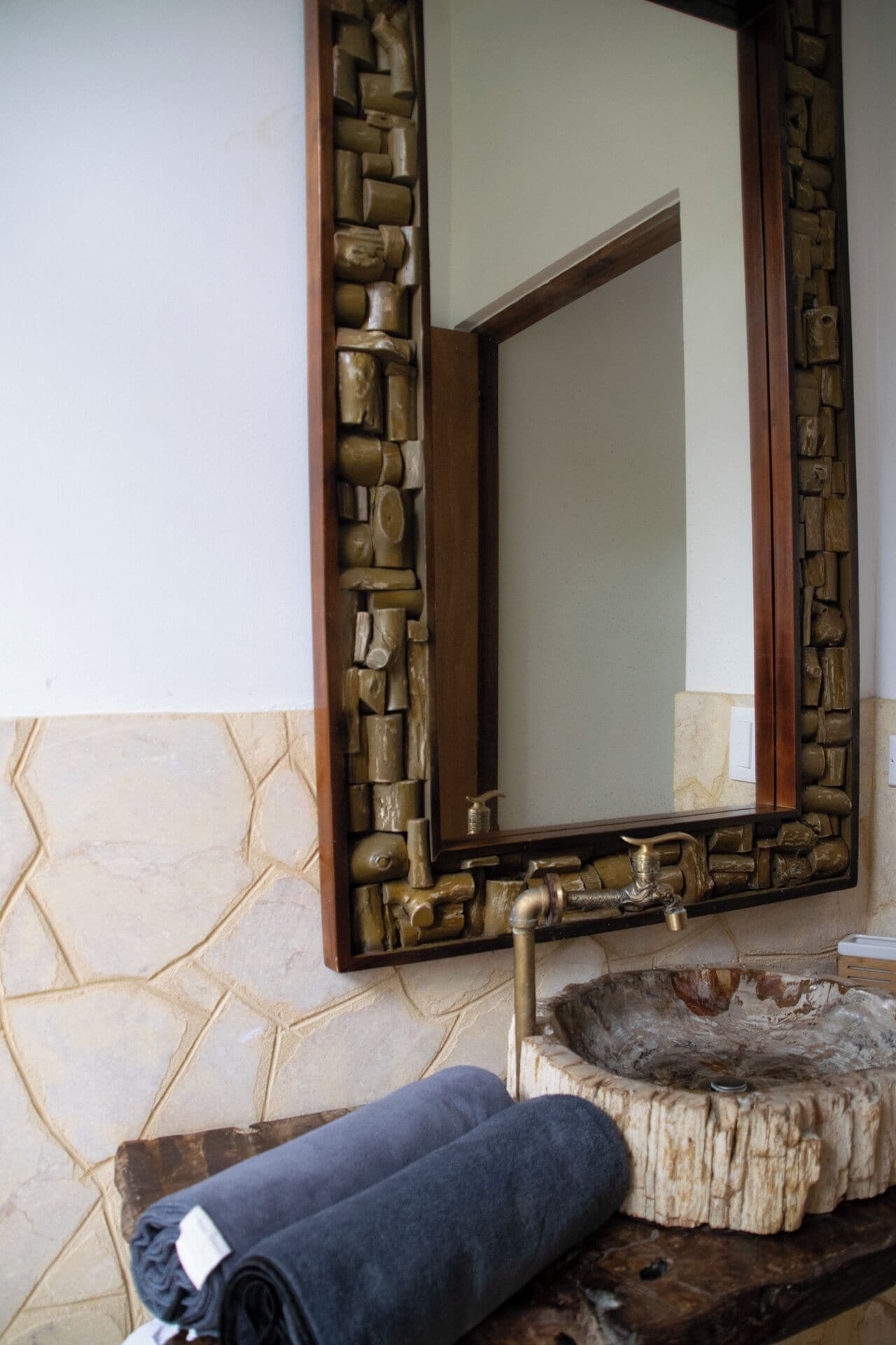 Ein Badezimmer mit einem Steinkonstruktion als Waschbecken, einem spiegelnden Wandbild mit Holzrahmen und einem Handtuch auf einer Holzbank.