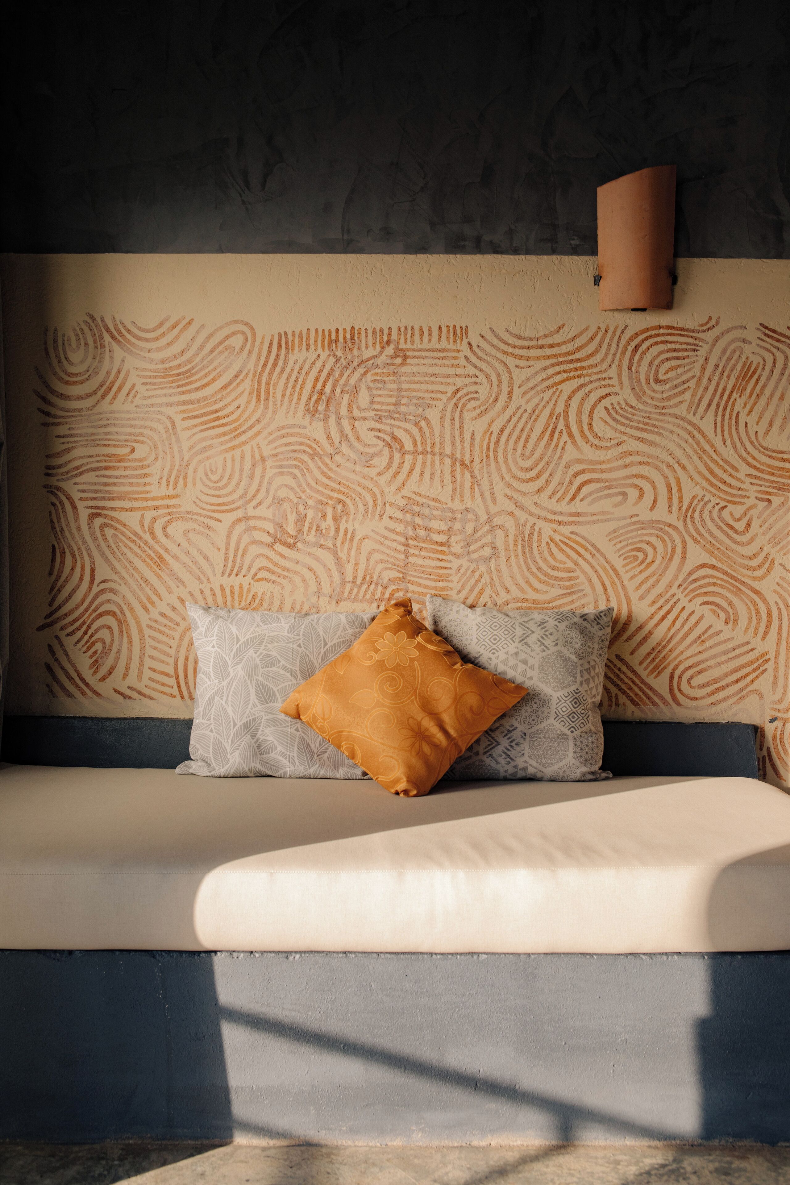 A bed with patterned wallpaper, a wall-mounted light, and two pillows.