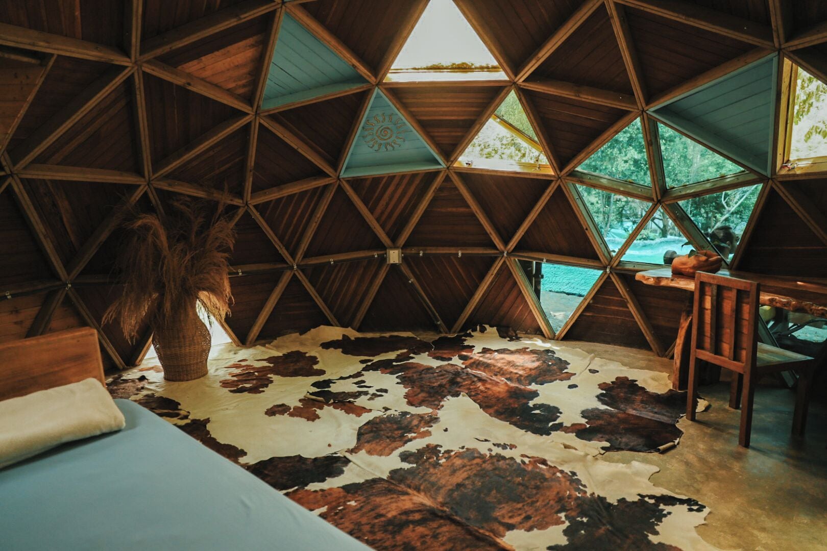Une pièce avec un plafond en bois aux motifs géométriques, un tapis en peau de vache, un lit et une table.
