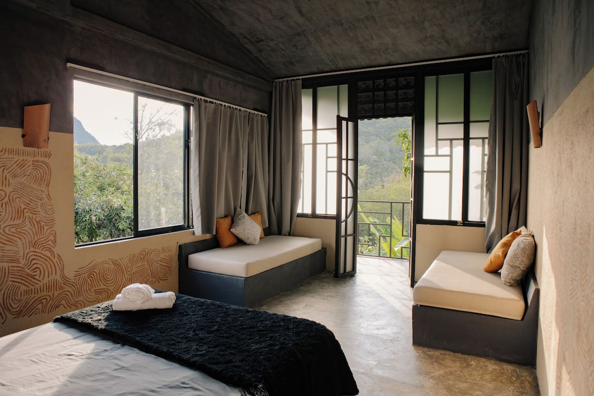 A bedroom with a large bed, two seating areas, and a view of greenery outside.