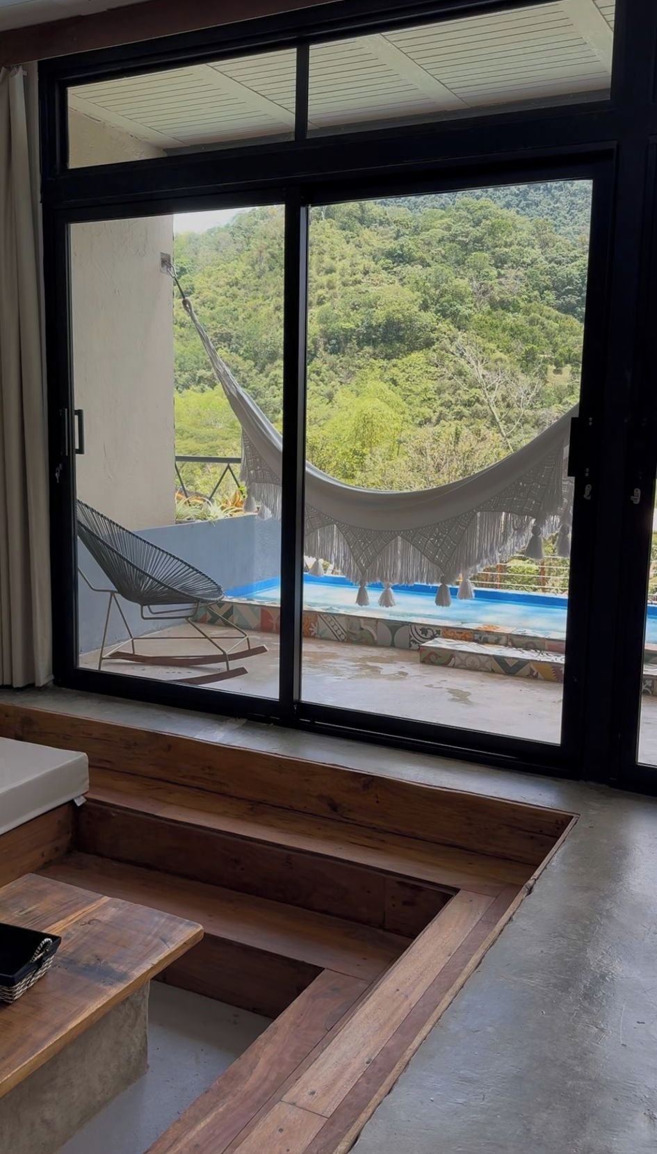 A room with a large sliding glass door leading to an outdoor area with a hammock and a pool.