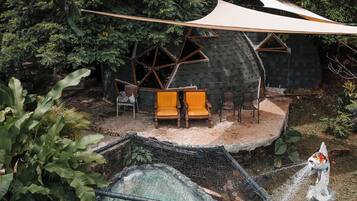 Una casa con techo inclinado, rodeada de un bosque denso. Cuenta con una piscina con cascada y un pequeño puente.