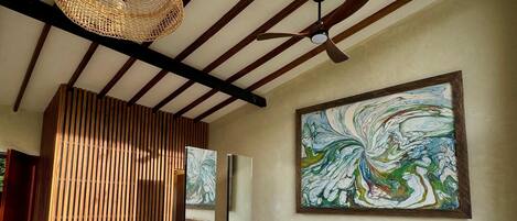 A modern bedroom with a bed, a ceiling fan, a large abstract painting, and a wooden slat partition.