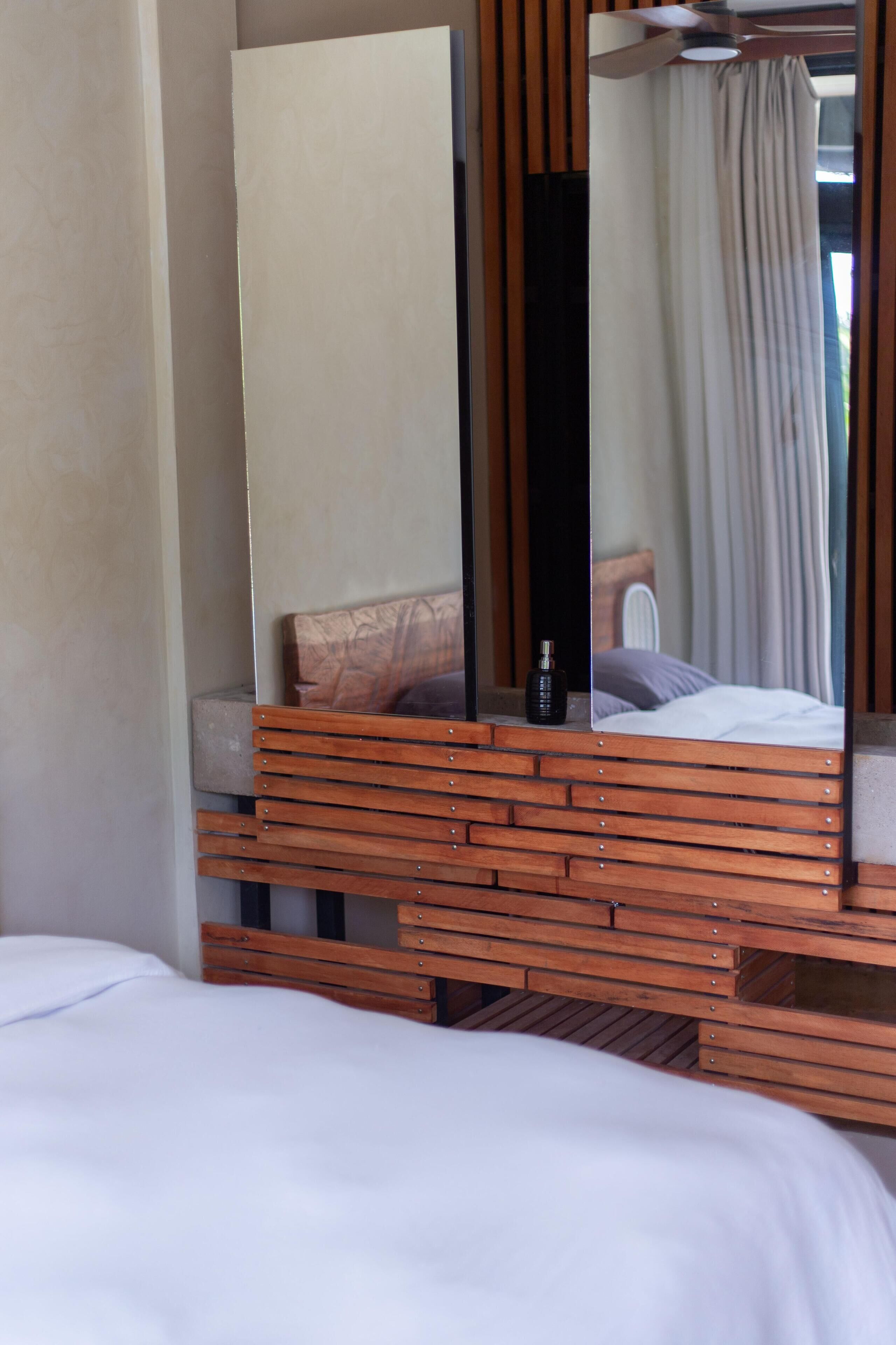 A bedroom with a wooden headboard, a large mirror, and a bed with white bedding.
