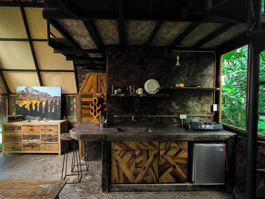 A rustic kitchen with a wooden counter, a small refrigerator, and a painting on the wall.