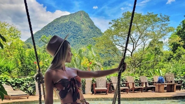 A person sitting on a swing by a pool with a mountainous backdrop. - Cerro Tusa Springs (Venecia)