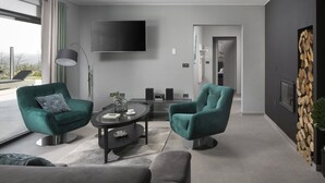 Uma sala de estar moderna com dois poltronas verde-água, uma mesa de centro e uma TV de tela plana fixada na parede.