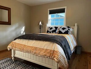 Cozy retreat with a neatly made bed, featuring a patterned bedspread and pillows, and a window with blinds.