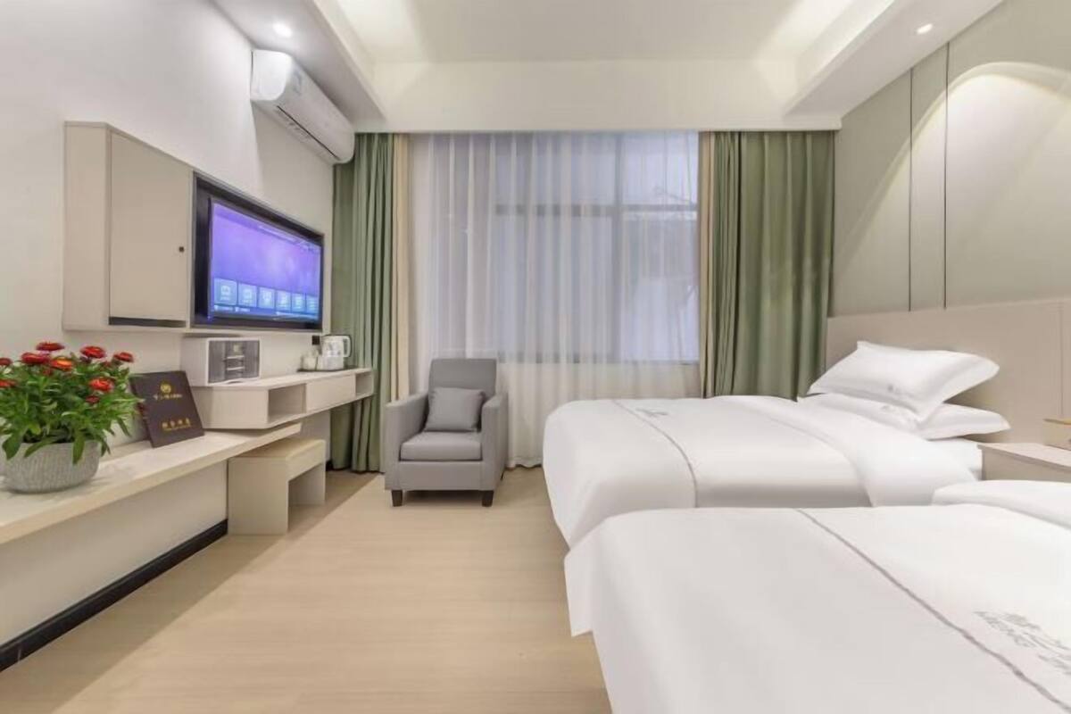 Une chambre d’hôtel avec deux lits, un téléviseur fixé au mur, un bureau avec un ordinateur et une chaise.