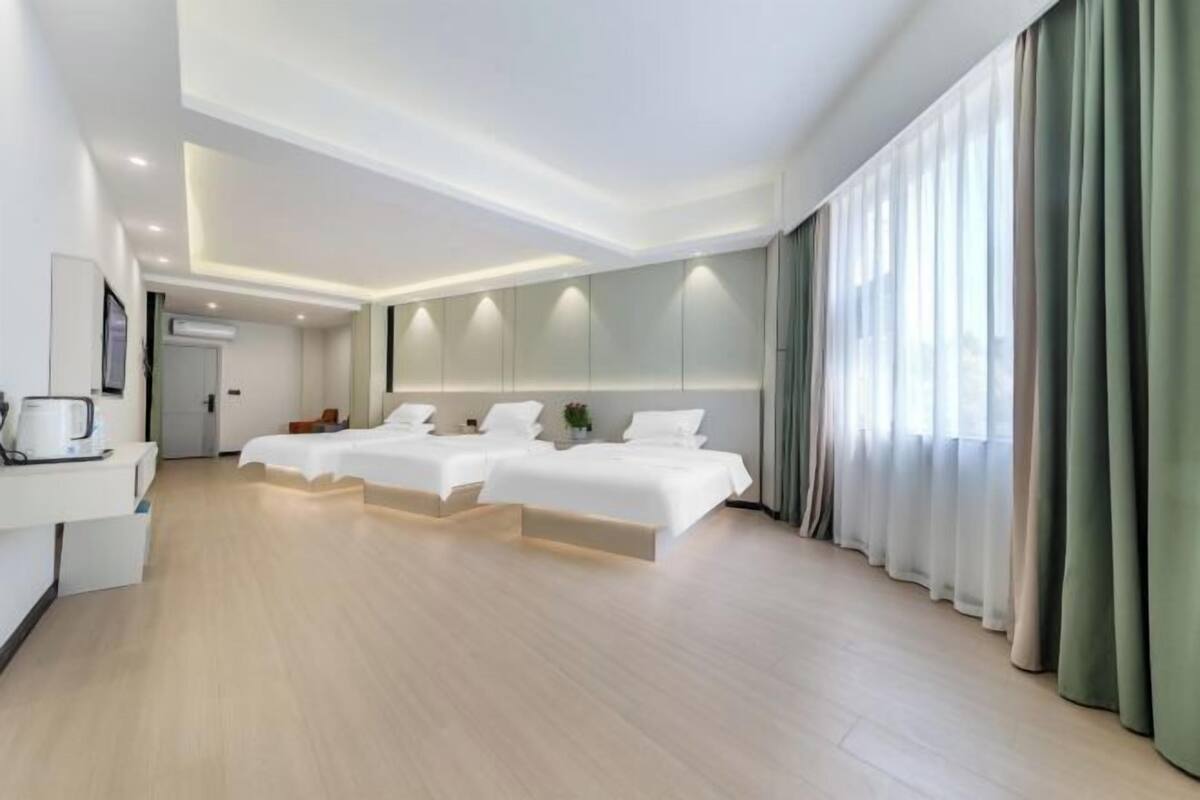 Une chambre d’hôtel moderne avec un grand lit, un bureau doté d’une machine à café et une grande fenêtre avec des rideaux.