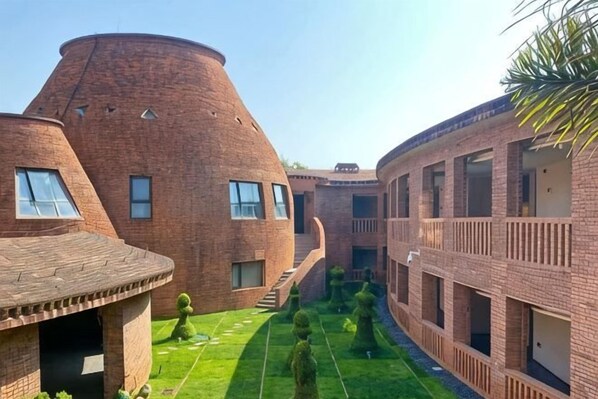 A courtyard with brick buildings, a central pathway, and a small tree.