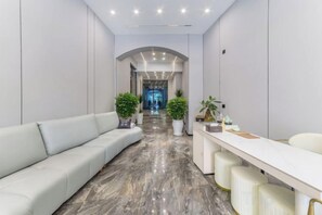 A modern hotel lobby with a curved reception desk, seating area, and a marble floor.