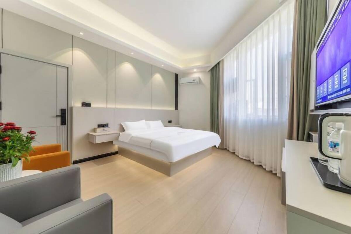 Une chambre d’hôtel moderne avec un grand lit, une télévision, une machine à café et une petite table agrémentée d’une plante.