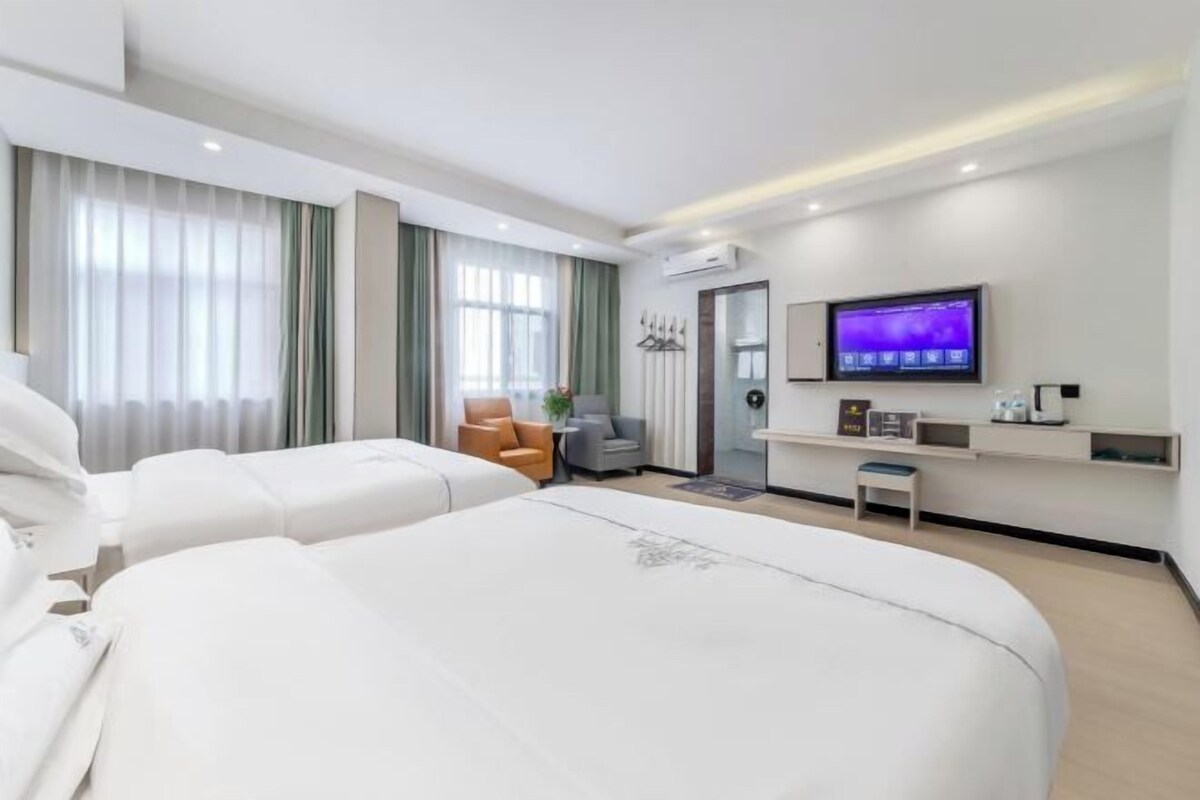 A modern hotel room with two large beds, a television, a small seating area, and a desk with a computer.