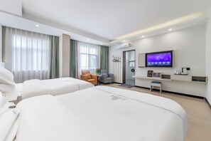 A modern hotel room with two large beds, a television, a small seating area, and a desk with a computer.