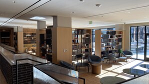 Una biblioteca moderna amb diversos nivells, prestatges, zones d'estar i grans finestres.