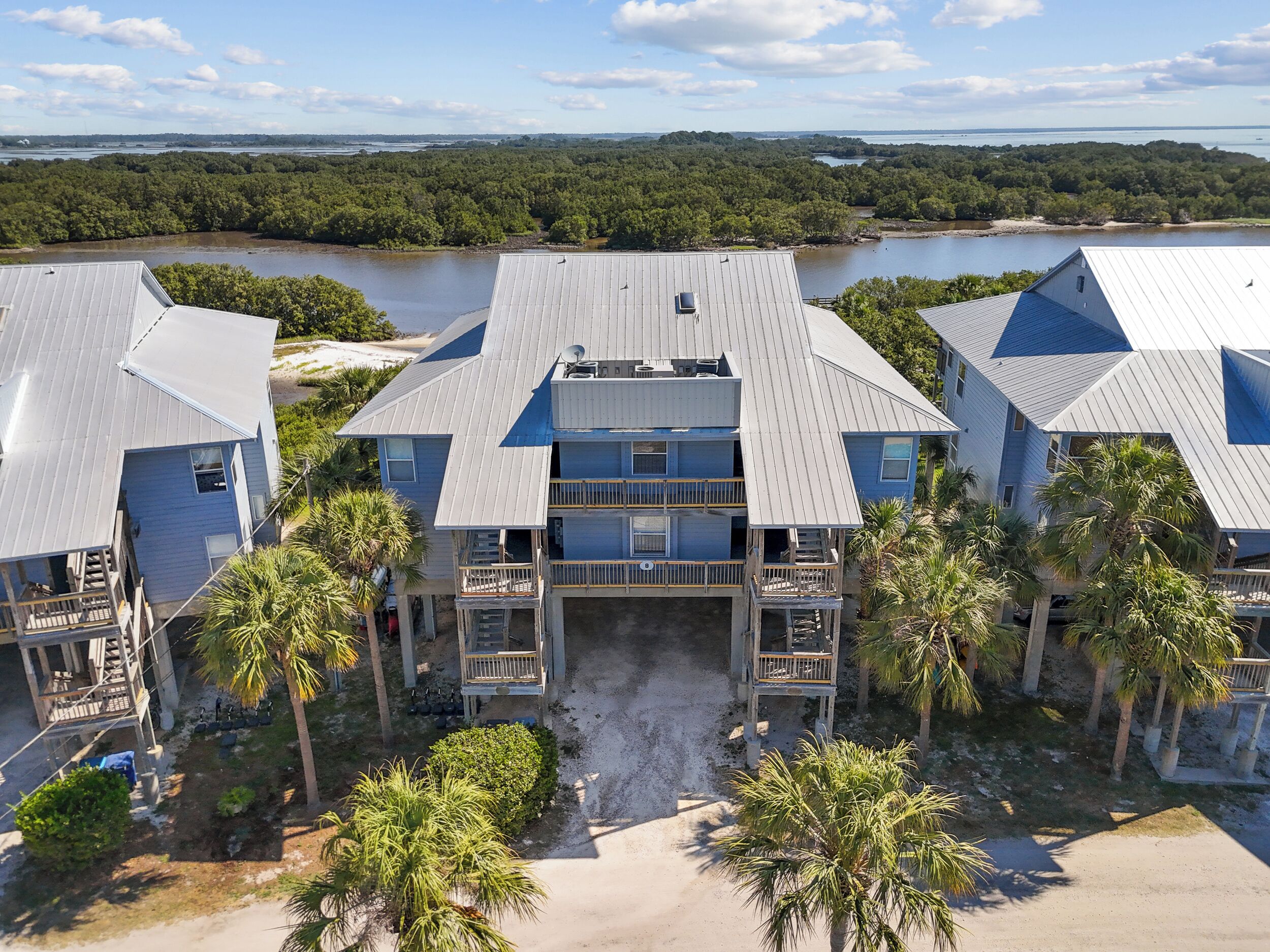 A multi-story building with a central courtyard, surrounded by palm trees and a body of water in the background.
