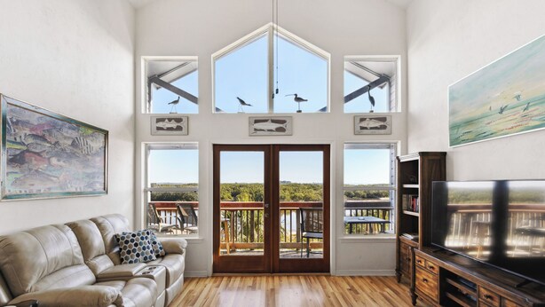 Een ruime woonkamer met een leren bank, houten vloeren, een grote televisie en een balkon met uitzicht op het landschap.