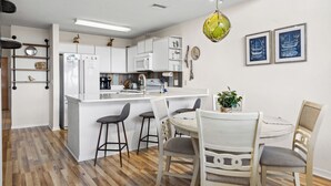 Een moderne keuken met witte kasten, een centraal eiland met krukken, en een eettafel met stoelen.