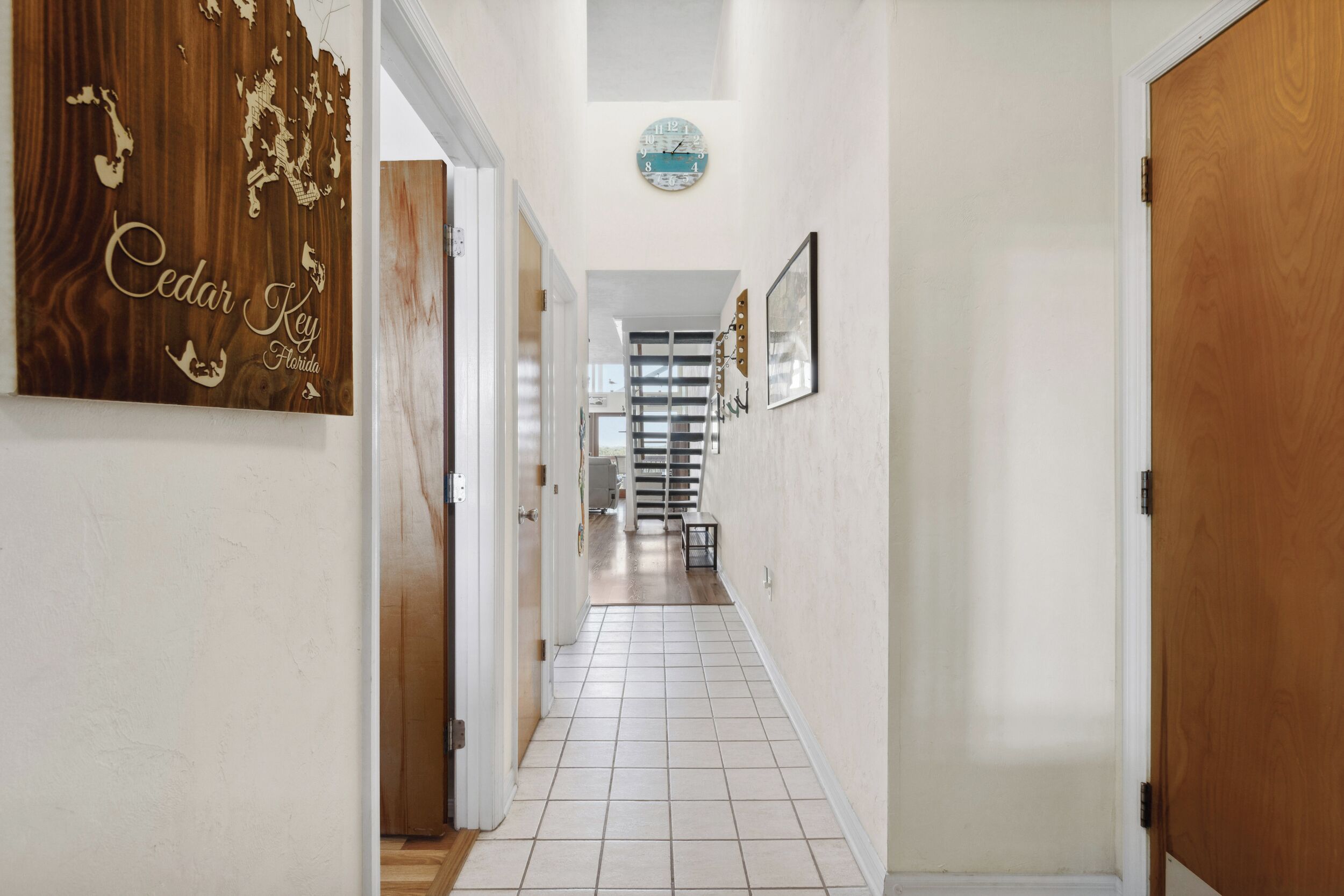 A hallway with a tiled floor, a wooden door on the right, and a wall with a 'Cedar Key Florida' sign.