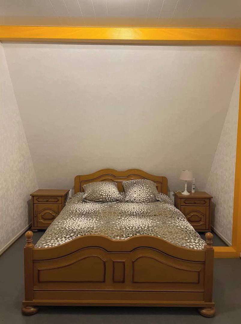 Een kleine kamer met een enkel bed, een houten hoofdeinde, twee nachtkastjes en een bed met een patroon.