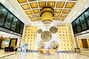 Um saguão com um lustre grande, um banco de madeira e uma parede com desenhos circulares.