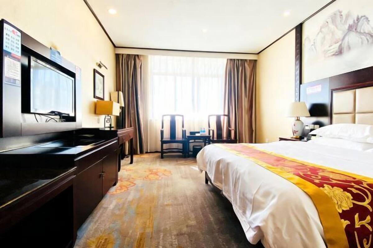Una habitación de hotel con cama, escritorio, silla, televisor y cortinas.