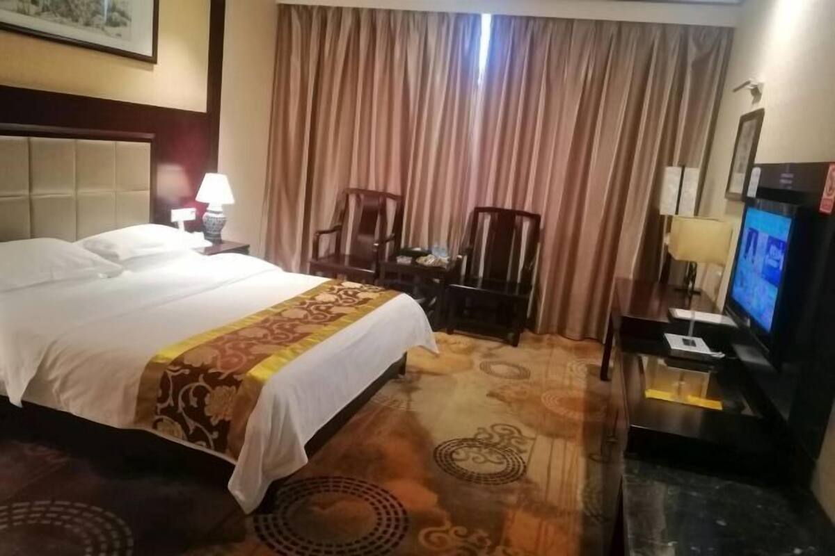 Habitación de hotel con cama, escritorio, computadora, televisor y cortina.