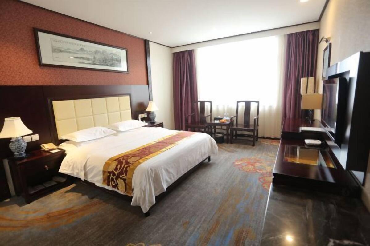 Una habitación de hotel con una cama grande, un escritorio, un televisor y una ventana con cortinas.