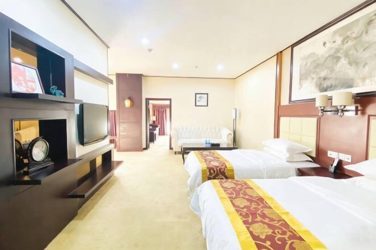 Una habitación de hotel con televisión, dos camas, un sofá, un escritorio y un cuadro en la pared.