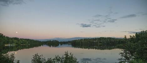 A serene lake at dusk with a clear sky and a visible moon.