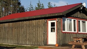Un edificio de madera con techo rojo, puerta blanca y una mesa de picnic en el exterior.