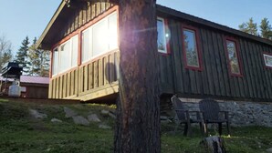 Una cabaña de madera con un porche, un muro de piedra y dos sillas afuera.