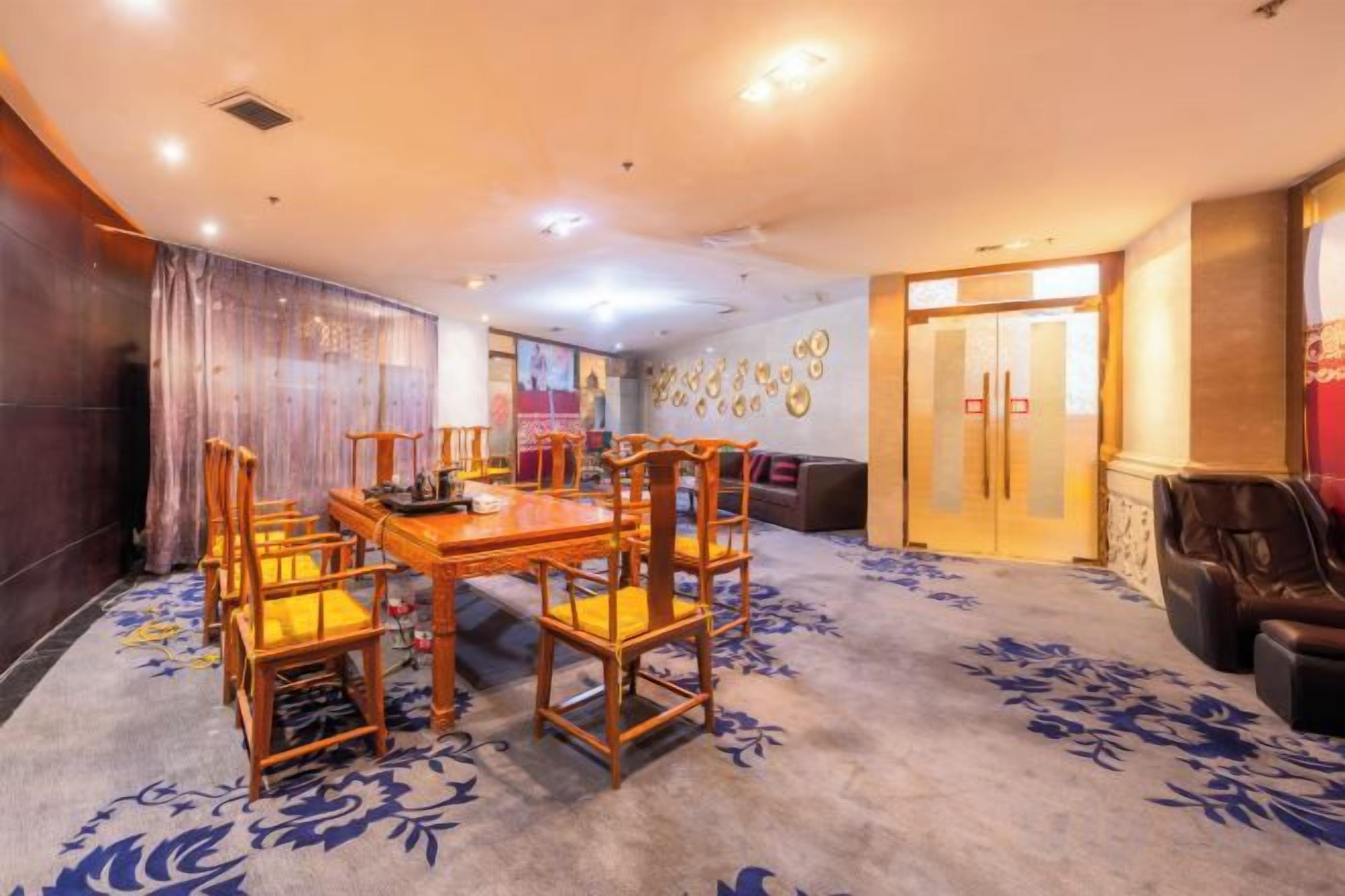 Een hotelconferentiezaal met een grote tafel en stoelen, een vloerkleed met een bloemmotief, en een muur met ronde decoraties.
