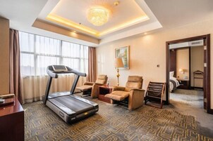 Habitación de hotel con caminadora, sillones reclinables, escritorio y un amplio ventanal.