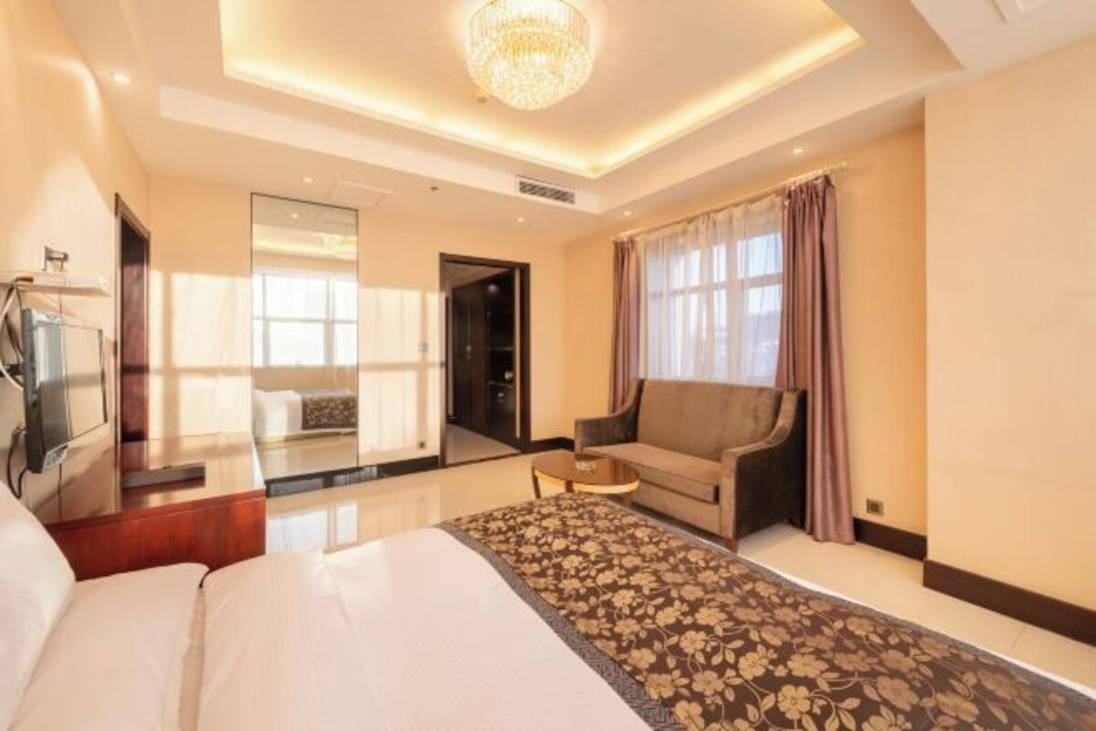 Een hotelkamer met een bed, een slaapbank, een tafeltje, een televisie en een kroonluchter.