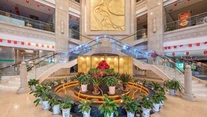 Un vestíbulo de hotel con un arreglo floral central, una gran obra de arte dorada en la pared y una zona de estar circular.