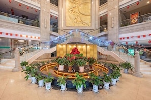 Un vestíbulo de hotel con un arreglo floral central, una gran obra de arte dorada en la pared y una zona de estar circular.