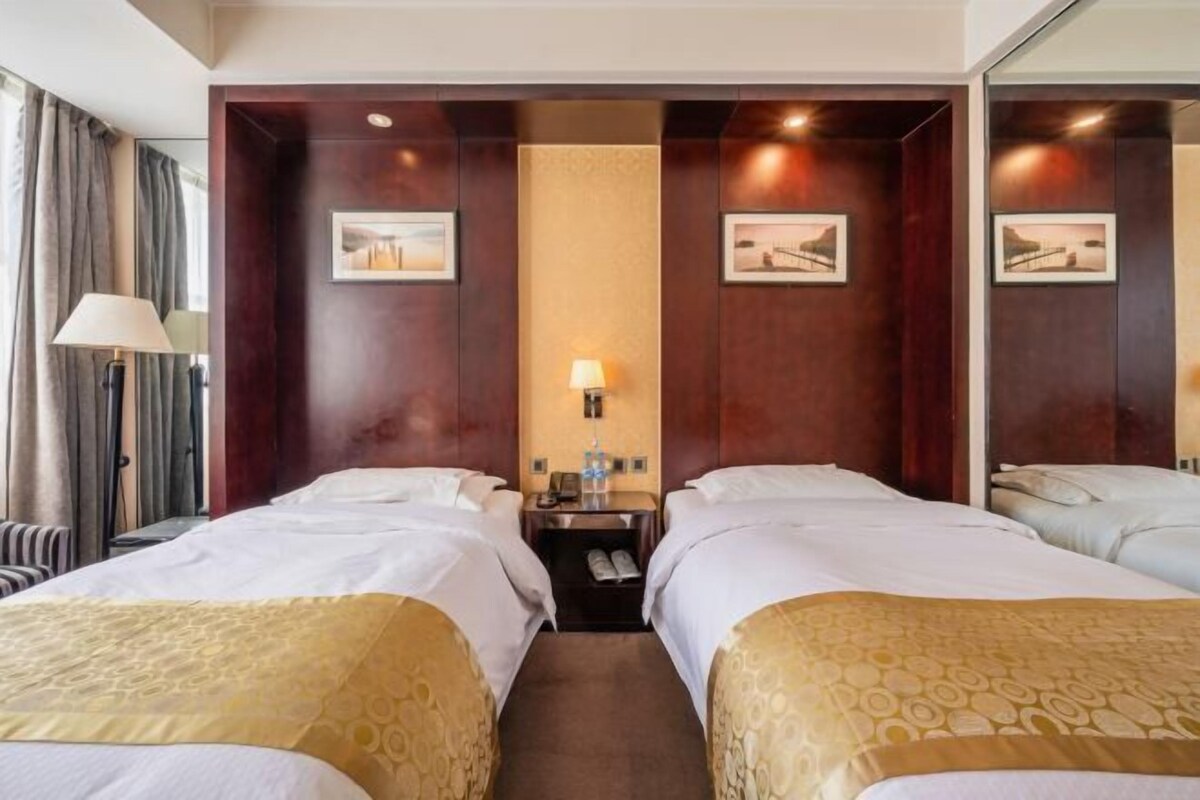 A hotel room with two beds, a nightstand, a lamp, and framed pictures on the walls.