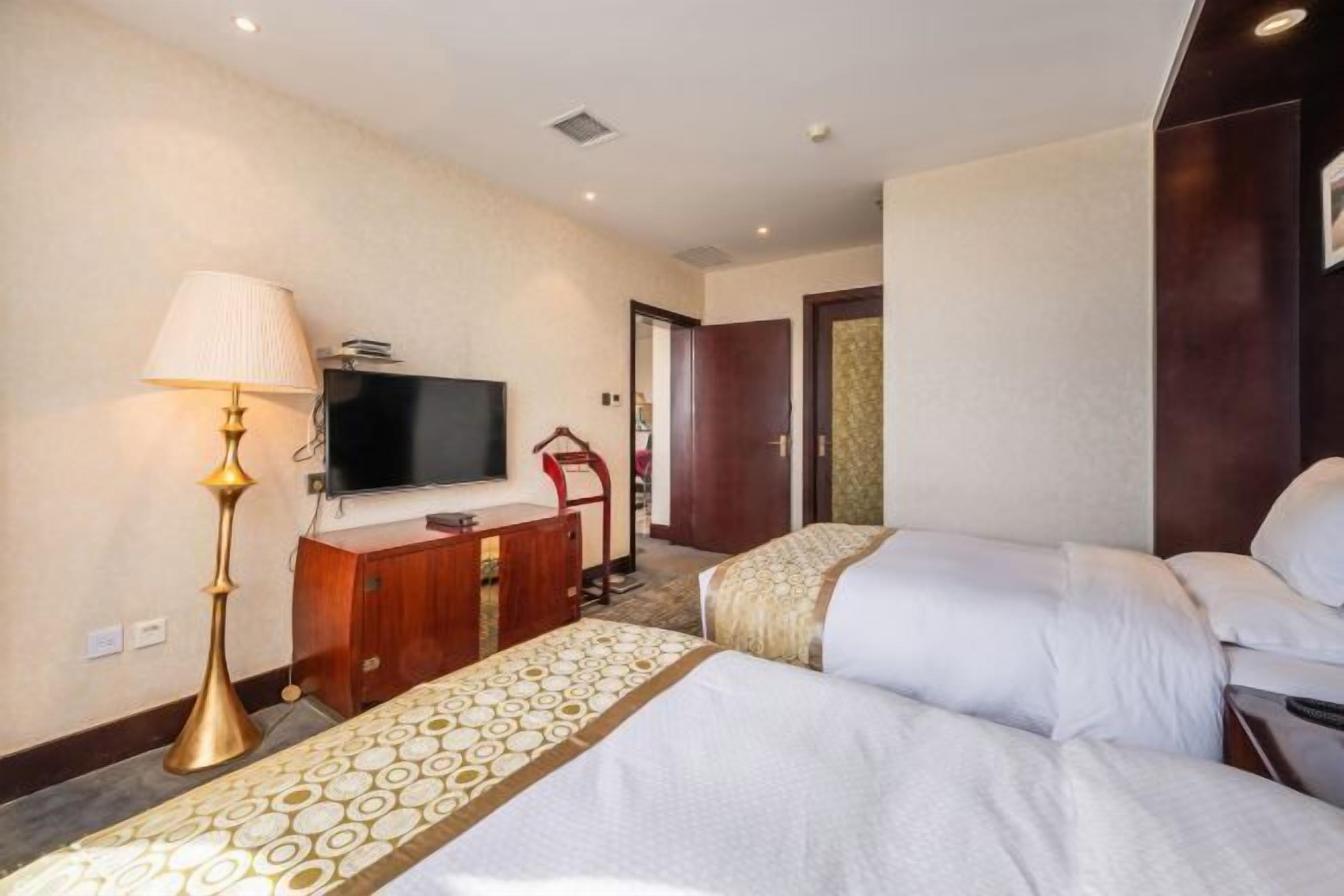 Une chambre d’hôtel avec deux lits, une télévision, un bureau, une lampe et une porte donnant sur une autre pièce.