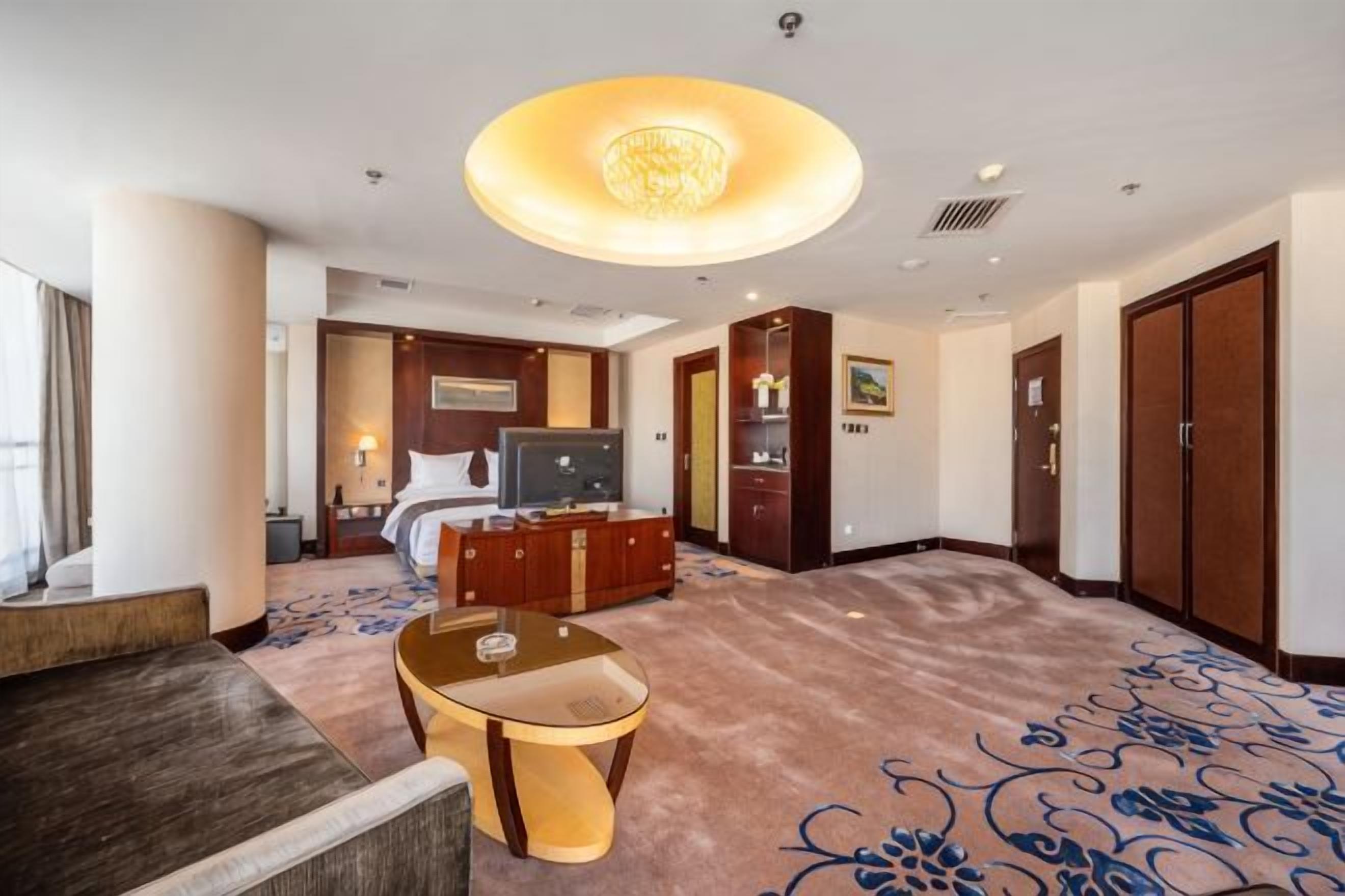 A hotel room with a large bed, a television, a desk, and a carpeted floor.